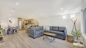 A modern living room with a grey sectional sofa, a coffee table, and a dining area with a table and chairs. - Brand New Canmore townhome (Canmore)