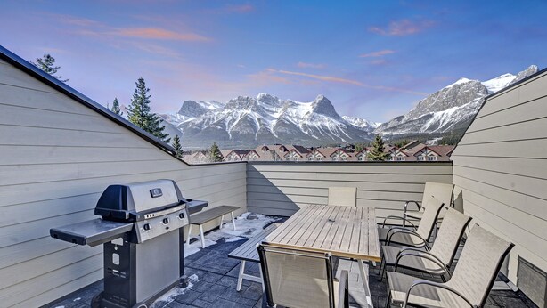 Une terrasse avec un barbecue, une table et des chaises, offrant une vue sur des montagnes enneigées.