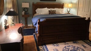 Ein Schlafzimmer mit einem hölzernen Bett, einem Nachttisch mit Lampe, einer Kommode und einem gerahmten Bild an der Wand.