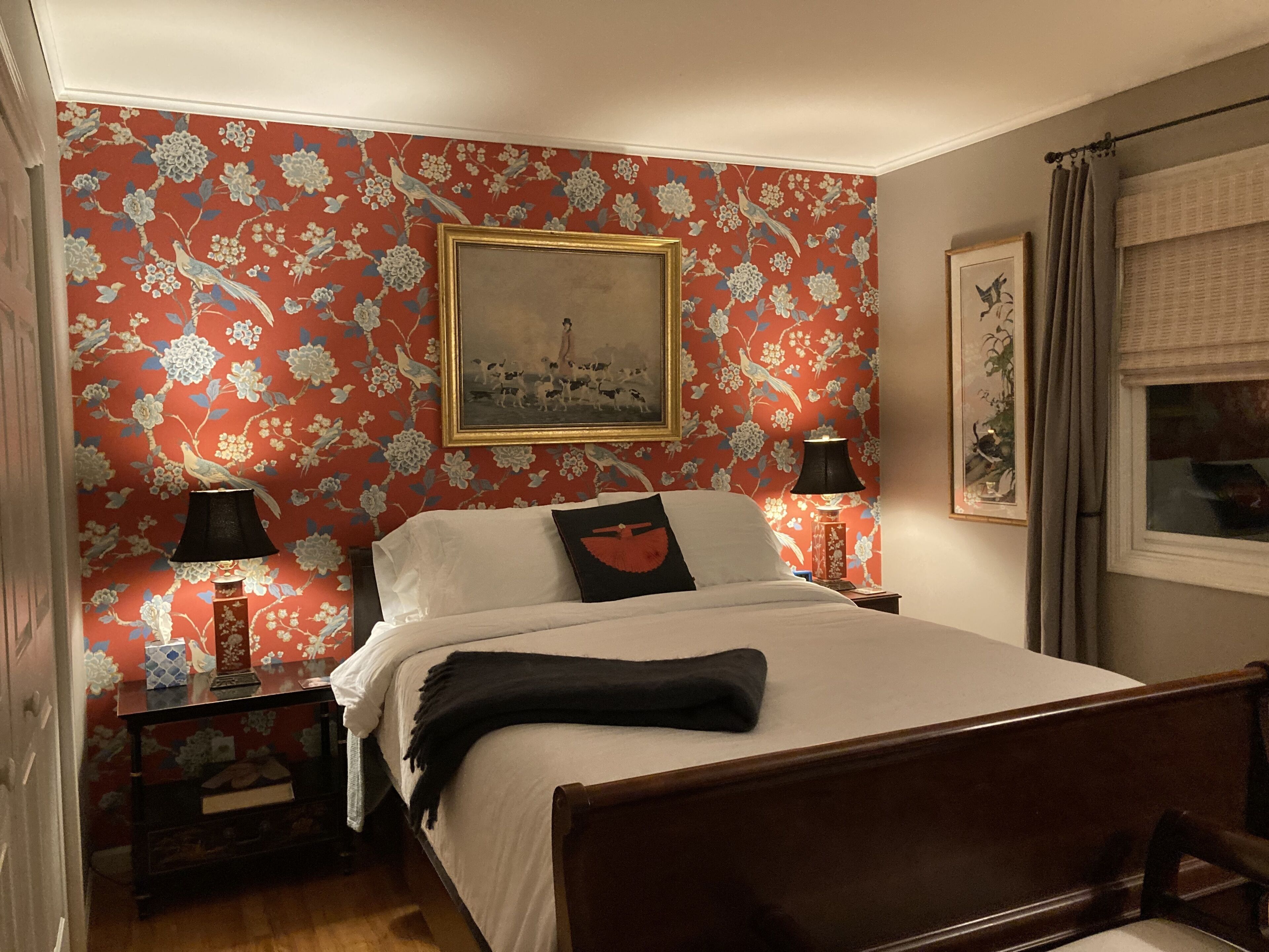 A bedroom with a floral wallpaper, a bed with white linens, two bedside tables with lamps, and a framed picture on the wall.