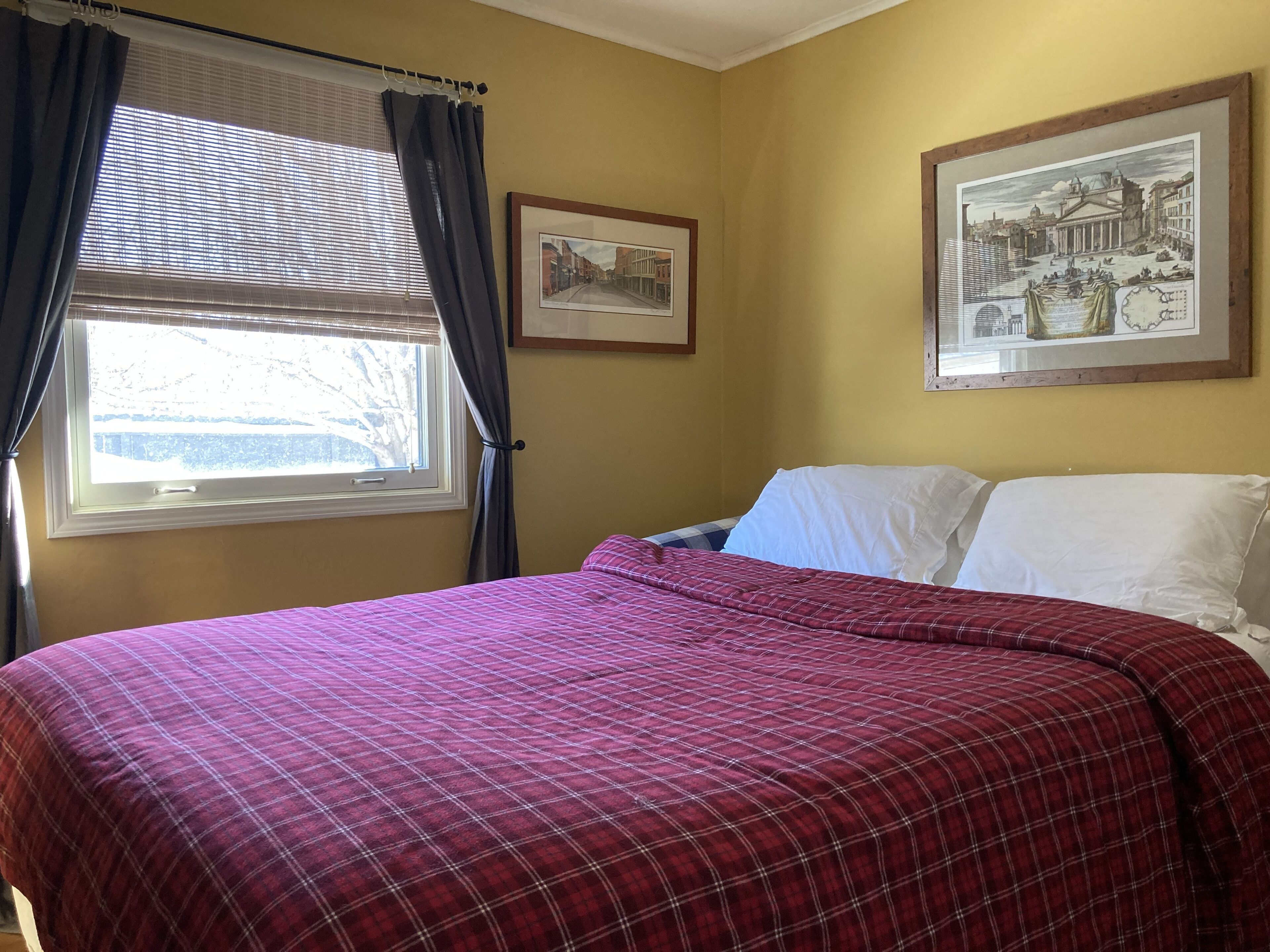 Une chambre à coucher avec un lit, une fenêtre avec des rideaux et deux tableaux encadrés accrochés au mur.