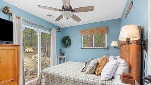 Une chambre à coucher avec un lit, un ventilateur de plafond, une télévision et une vue sur l’extérieur.