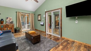 Un salon doté d’un ventilateur de plafond, d’un téléviseur à écran plat fixé au mur, d’une table basse en bois, d’un canapé et d’une porte-fenêtre coulissante donnant sur un balcon.