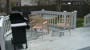 Une terrasse avec un barbecue, deux fauteuils en osier et une table en verre.