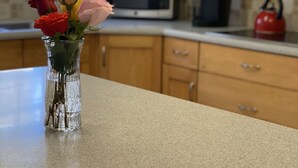 A kitchen with wooden cabinets, a microwave, a kettle, and a vase with flowers on the countertop. - Amazing Property Close To Beaches/Golf Course/Railway Trails (Warwick)