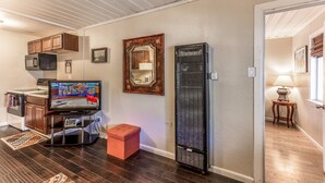 Een woonkamer met een televisie, een magnetron, een kast, een lijstspiegel, een heater en een klein krukje.