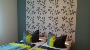 Un lit double avec deux oreillers, une table de chevet et un mur orné d’un motif de feuilles.