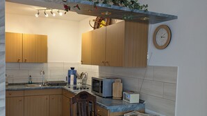 Une cuisine moderne avec des meubles en bois, un plan de travail en marbre, un coin repas avec une table et des chaises, et une horloge au mur.