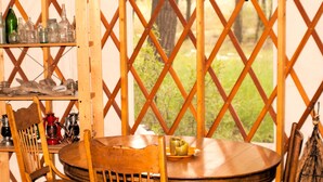 Une table de salle à manger en bois, avec des chaises, une assiette remplie de nourriture et une fenêtre ornée d’un motif en treillis.