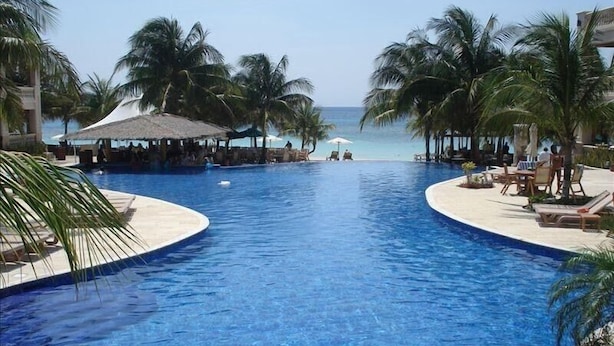 A pool with a view of the ocean, surrounded by palm trees and lounge chairs. - INFINITY BAY LUXURY 2/2 condo,100 steps to beach, 2nd story, by pool,1388 sqft   (West Bay)