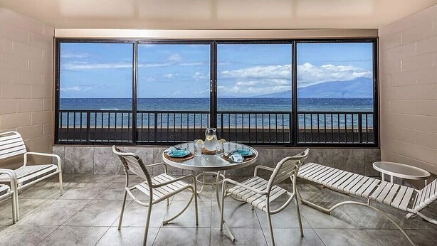 A balcony with a view of the sea, a round table with chairs, and a small table with a pitcher and glasses. - Oceanfront, adjacent to North Ka'anapali Beach, Central A/C! Newly reduced rates (Lahaina)