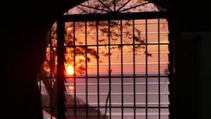 Une fenêtre ornée d’une grille métallique, à travers laquelle on peut admirer un coucher de soleil.