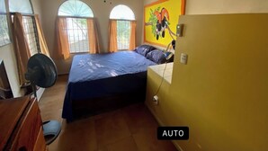 Une chambre à coucher comprenant un lit, un ventilateur de plafond, un appareil de climatisation et une fenêtre avec des rideaux.
