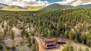 Un chalet accessible par un chemin de terre, entouré d’une forêt dense et de montagnes.