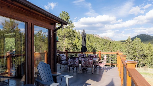 Une terrasse en bois, agréée de mobilier d’extérieur comprenant des chaises et des tables, qui offre une vue sur une zone boisée avec des montagnes en arrière-plan.