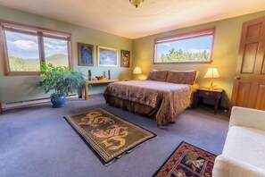A bedroom with a bed, two windows, a potted plant, a nightstand, a lamp, and a rug.