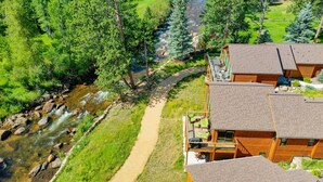 A lodge with multiple wooden cabins, a river running through the property, and a dirt path leading to the cabins.