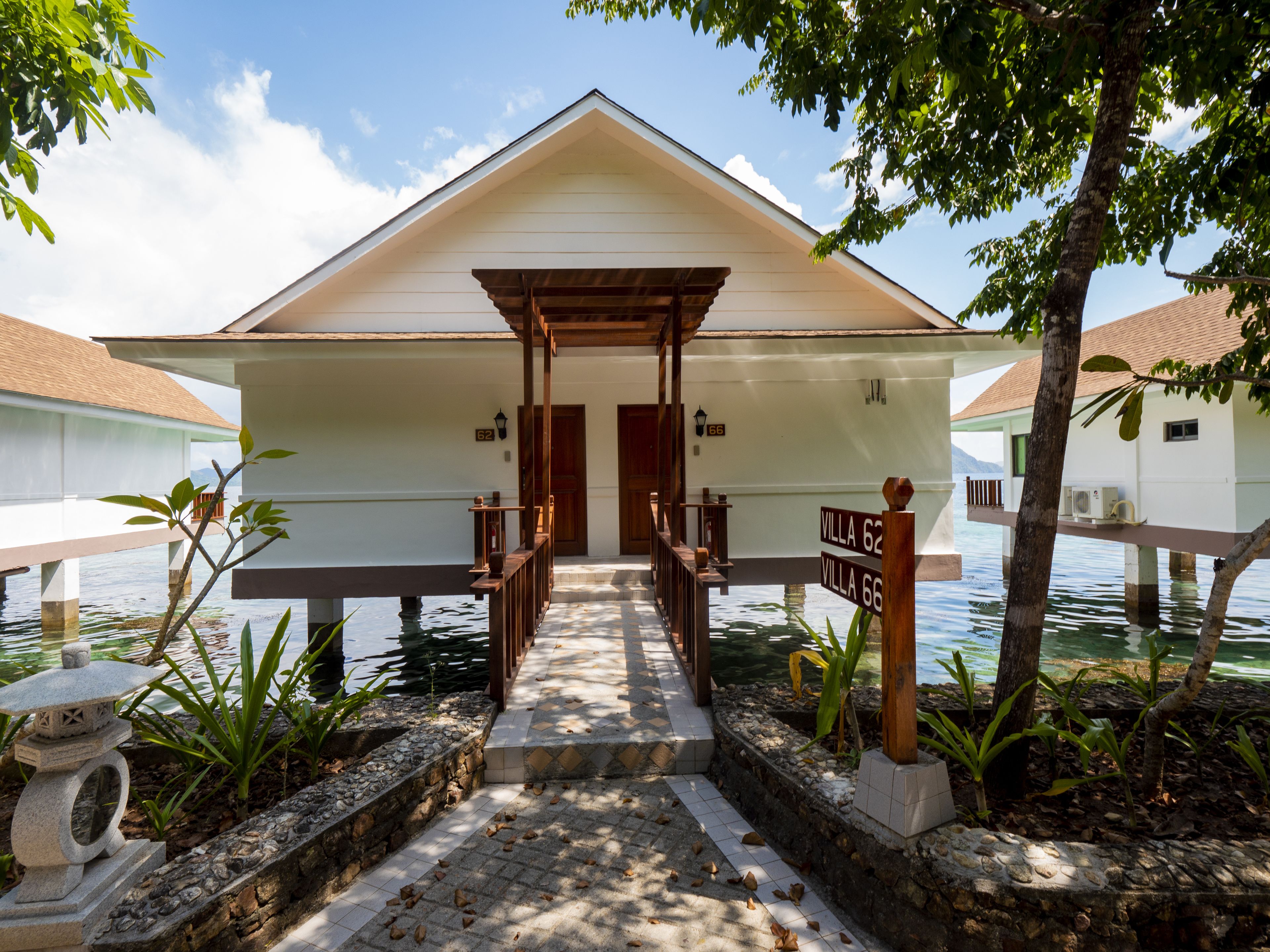 A villa with a covered entrance, a stone pathway, and a water body in the background.