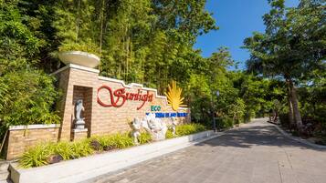 A sign for Sunlight Eco Resort with a sun emblem, surrounded by lush greenery and a paved pathway.