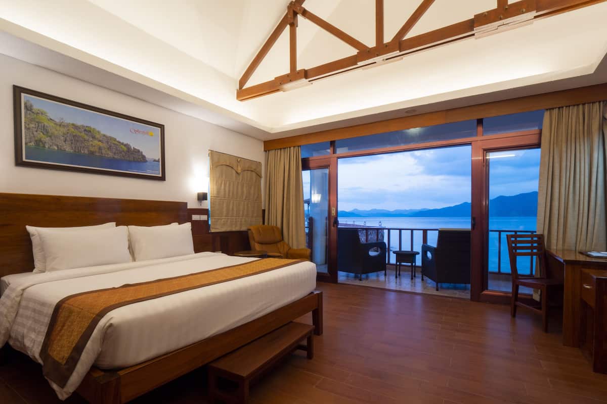 Une chambre d’hôtel avec un grand lit, un bureau avec des chaises et un balcon donnant sur la mer.