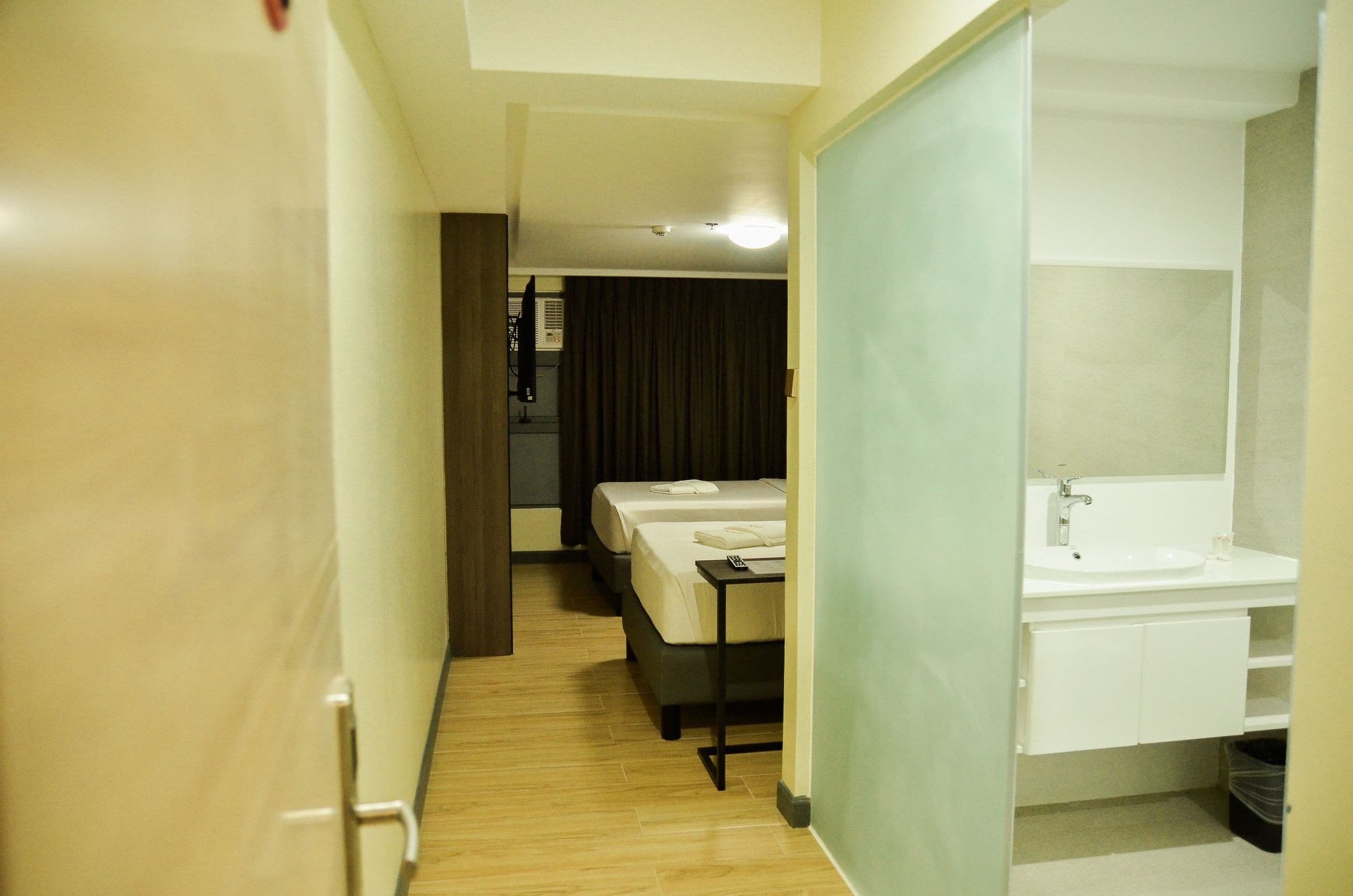 Une chambre d’hôtel avec un plancher en bois, un lit, un bureau et une salle de bain équipée d’un lavabo et d’un miroir.