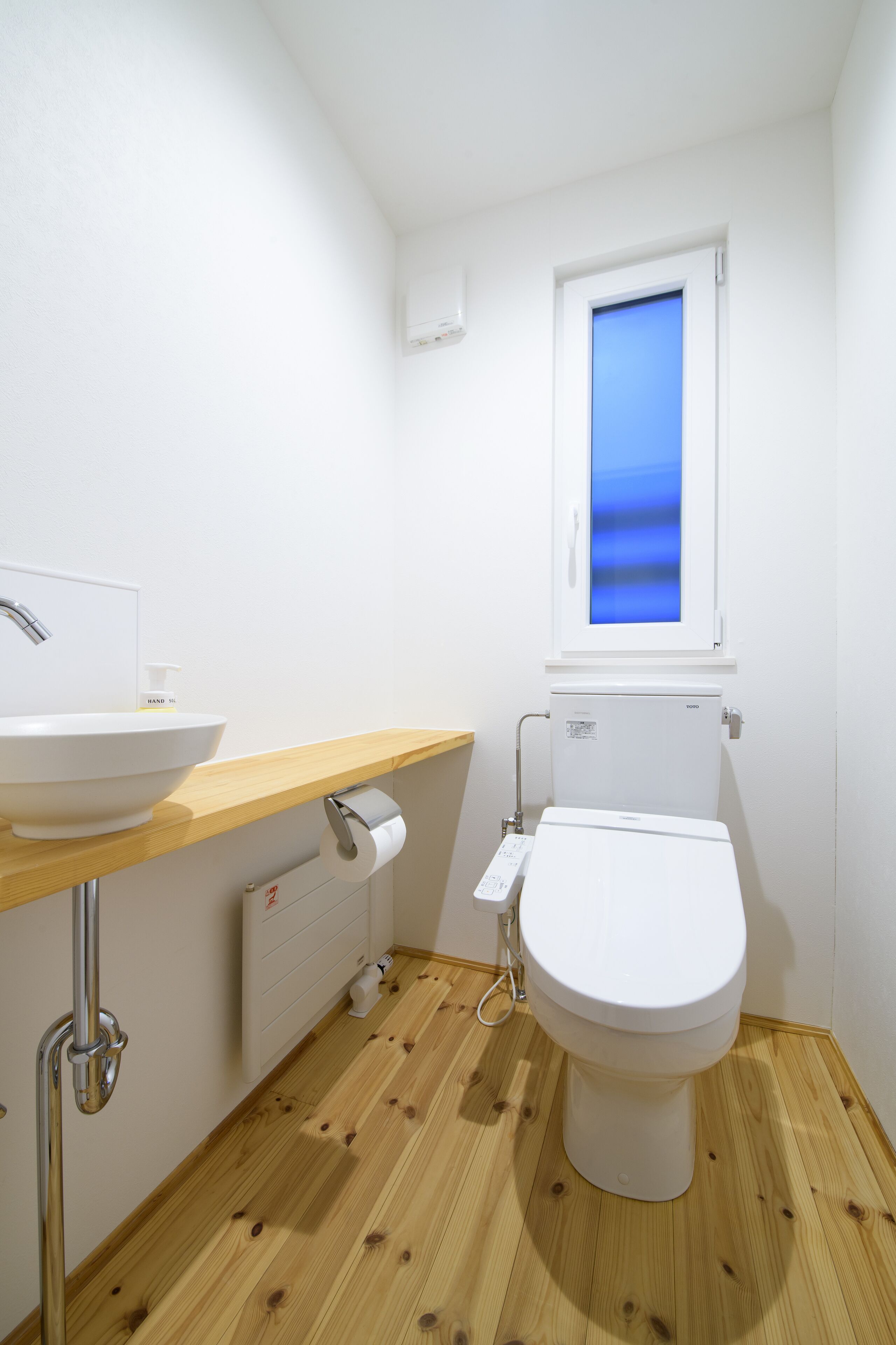 A small, modern bathroom with a white sink, toilet, and wooden flooring.