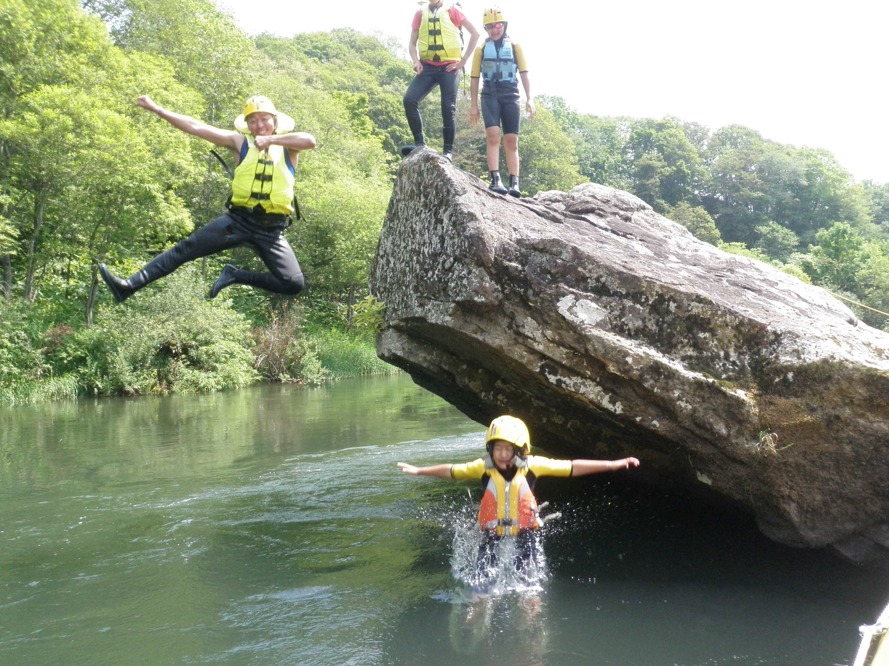 A group of people jumping off a large rock into a river.