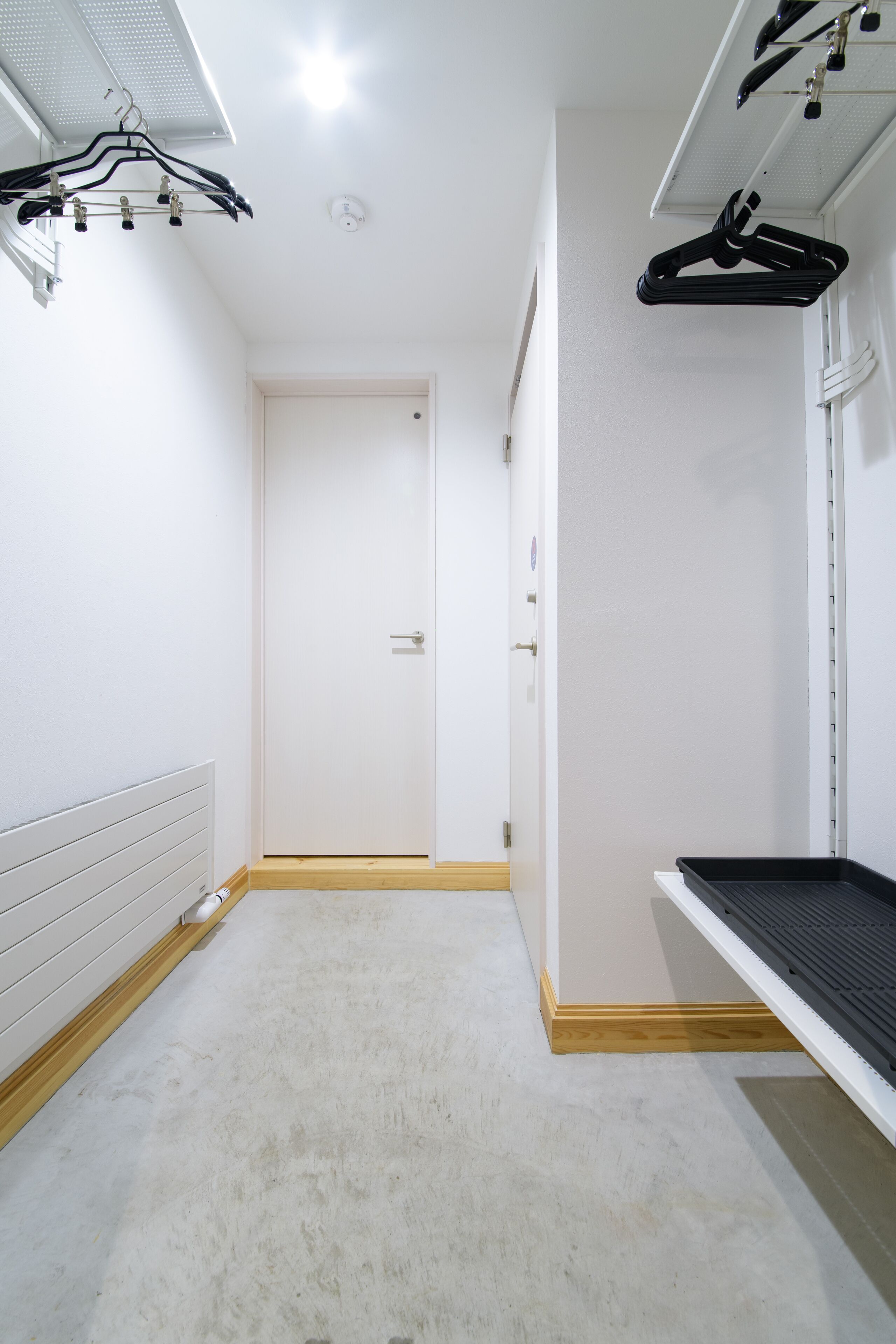 Un couloir avec une porte blanche, un radiateur et une étagère noire.