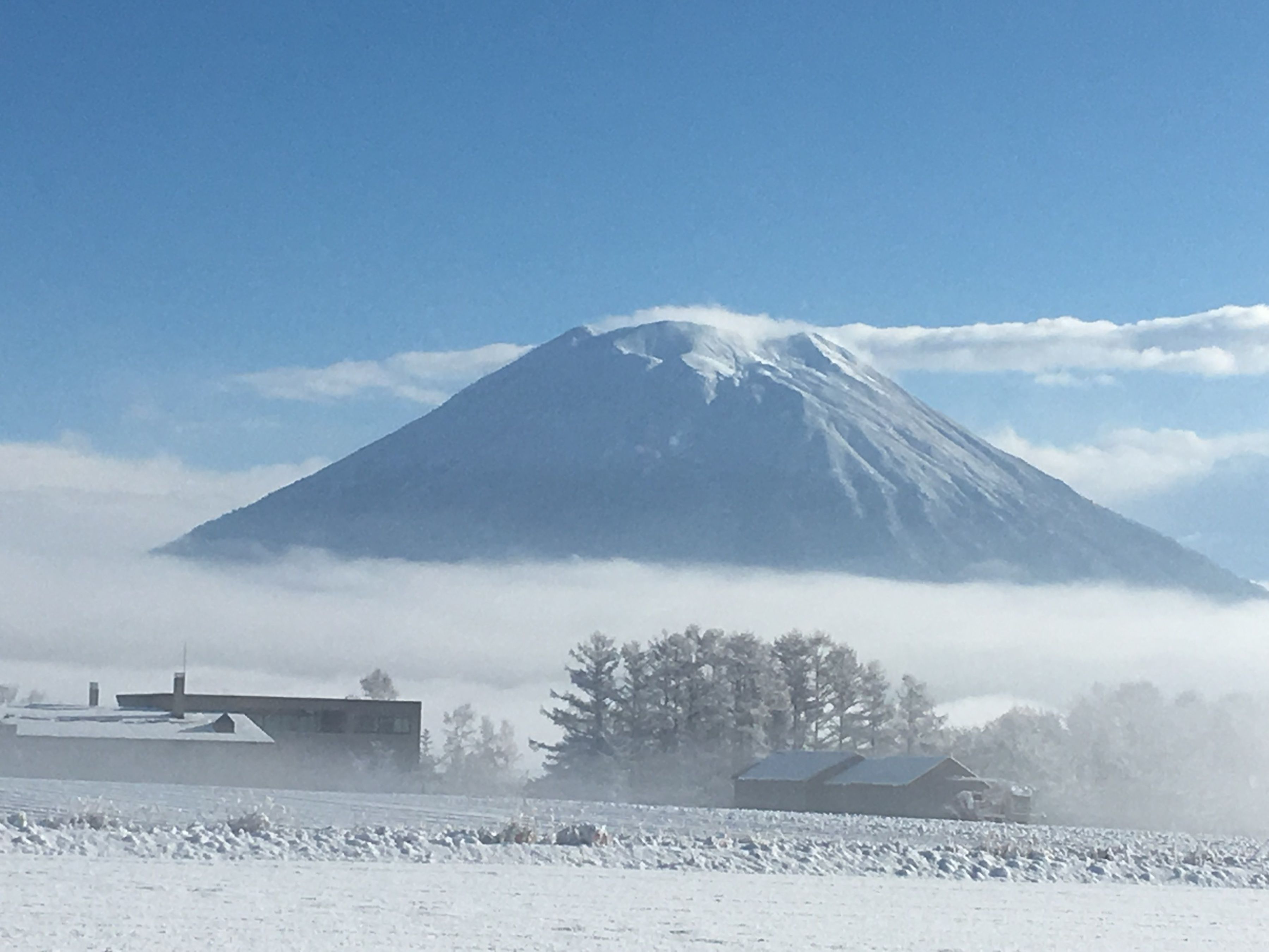 A snow-covered landscape with a prominent mountain and a few buildings in the foreground.