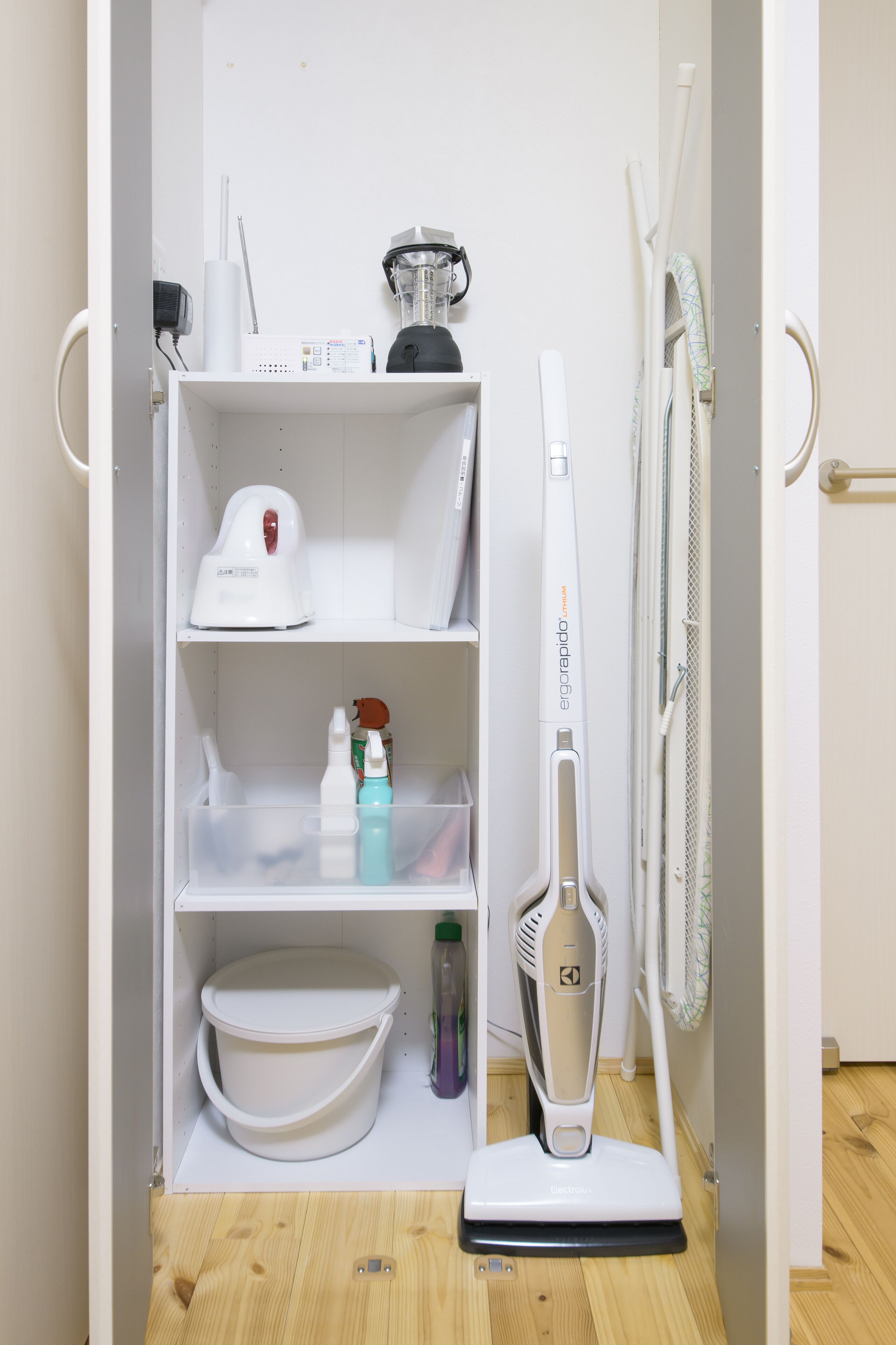 Un mueble blanco con una licuadora, una tetera, un aspirador y un estante con un tazón y productos de limpieza.