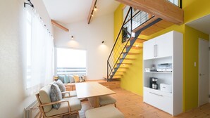A modern kitchen with wooden flooring, a dining area with a table and chairs, a staircase, and a white cabinet with appliances. - Niseko Highland Cottages (Niseko)