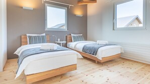 A modern bedroom with two beds, wooden flooring, and large windows providing natural light. - Niseko Highland Cottages (Niseko)