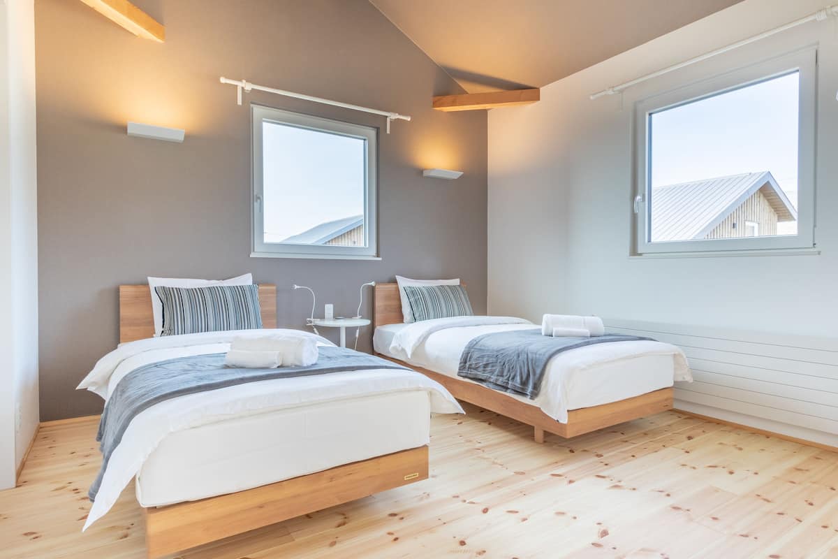 Une chambre moderne avec deux lits, un plancher en bois et de grandes fenêtres qui laissent entrer la lumière naturelle.