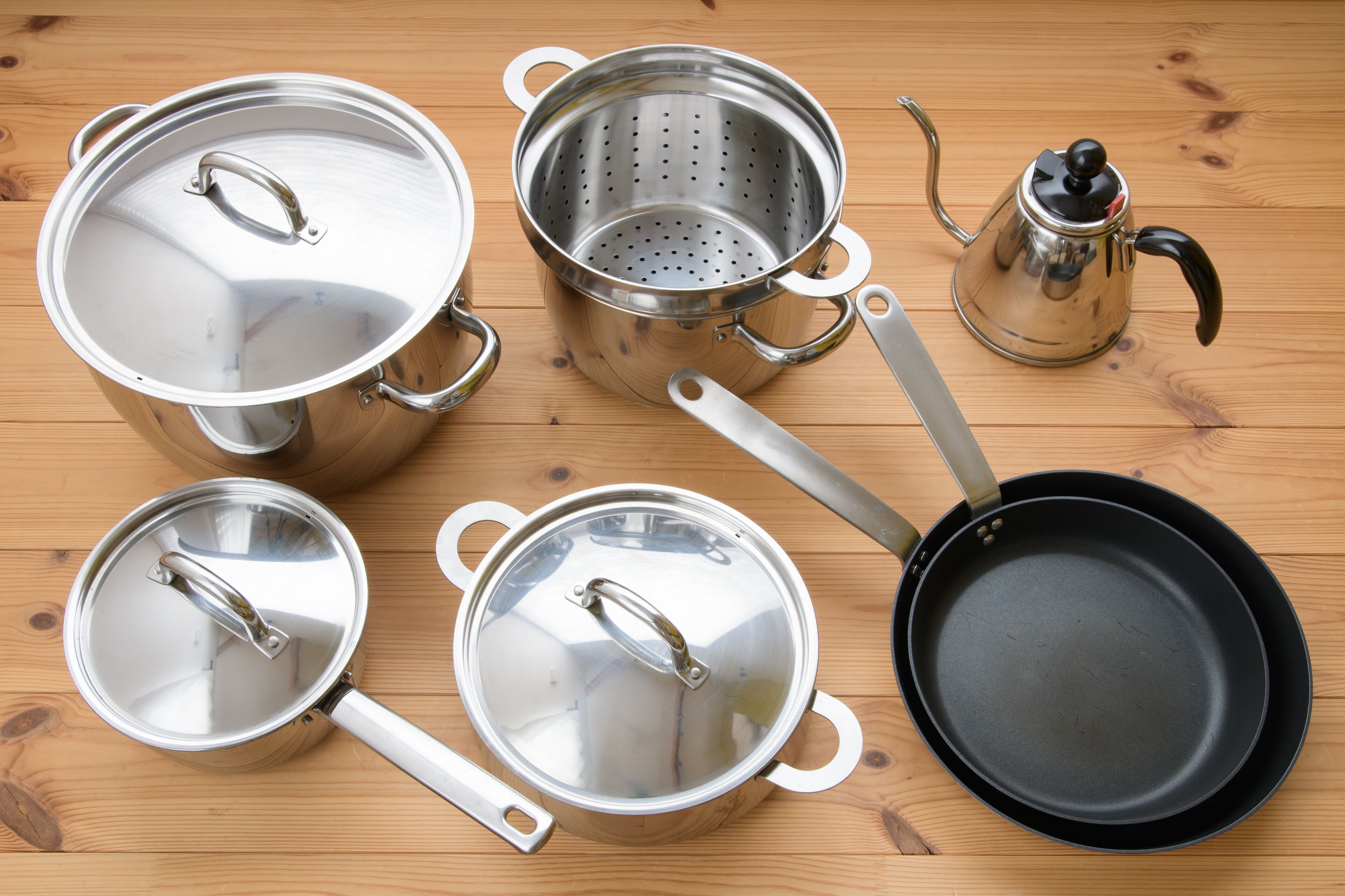 A set of stainless steel cookware including pots, a pan, and a colander on a wooden surface.