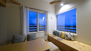 A cozy room with a wooden dining table, a bench with cushions, and large windows offering a view of the outdoors. - Niseko Highland Cottages (Niseko)