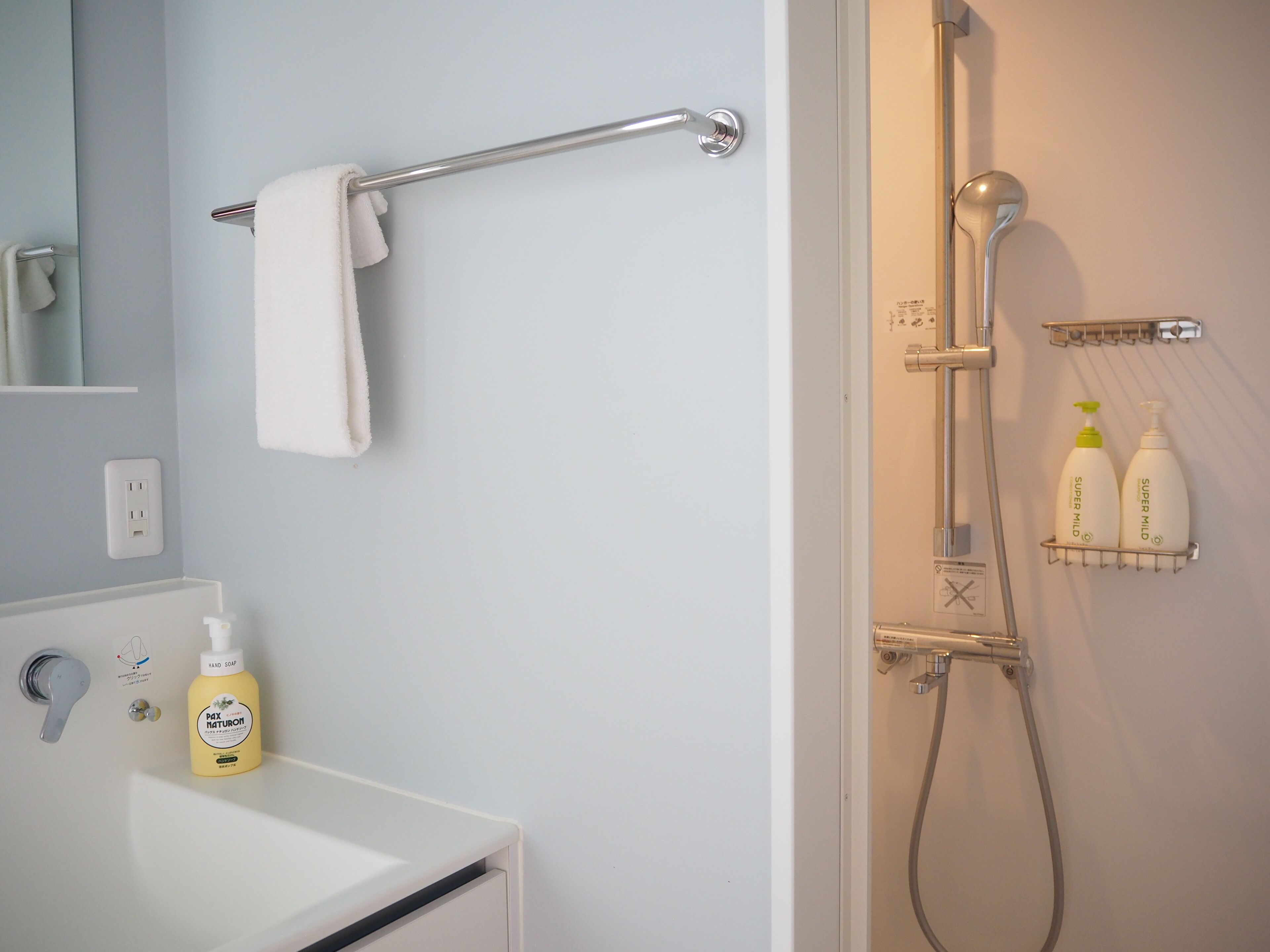A bathroom with a white sink, a towel rack, a shower with a handheld showerhead, and two bottles of hand soap on the wall.