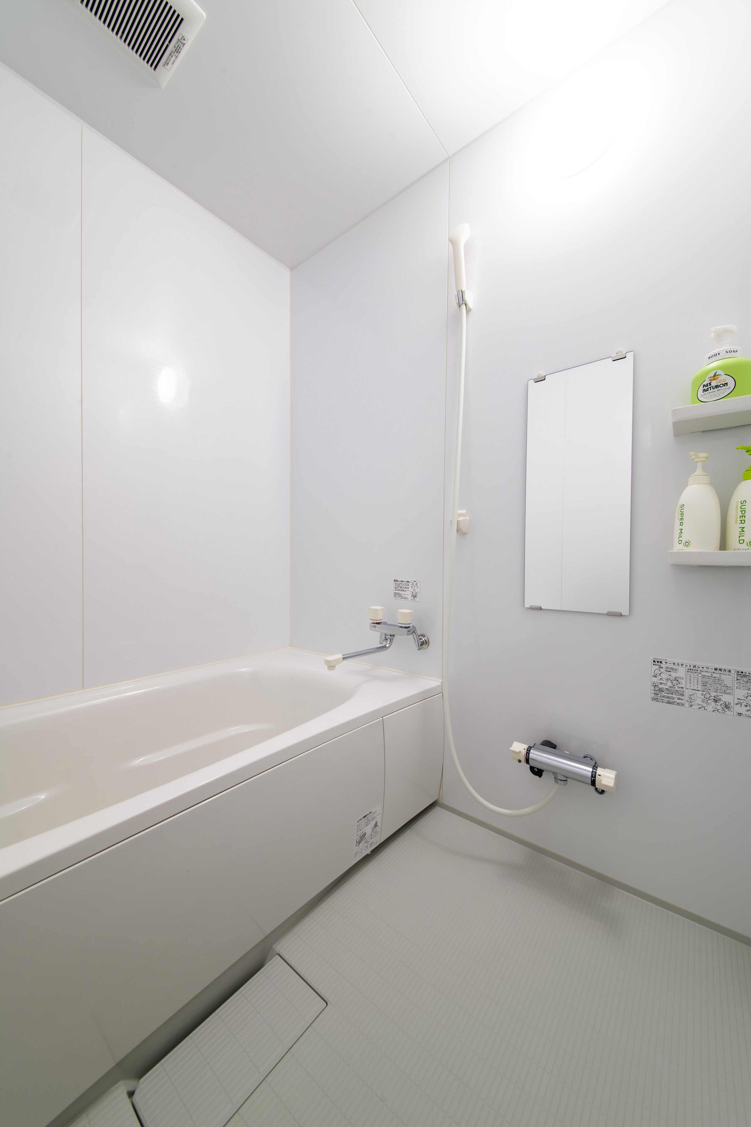 A modern bathroom with a white bathtub, a wall-mounted mirror, and a shelf with toiletries.
