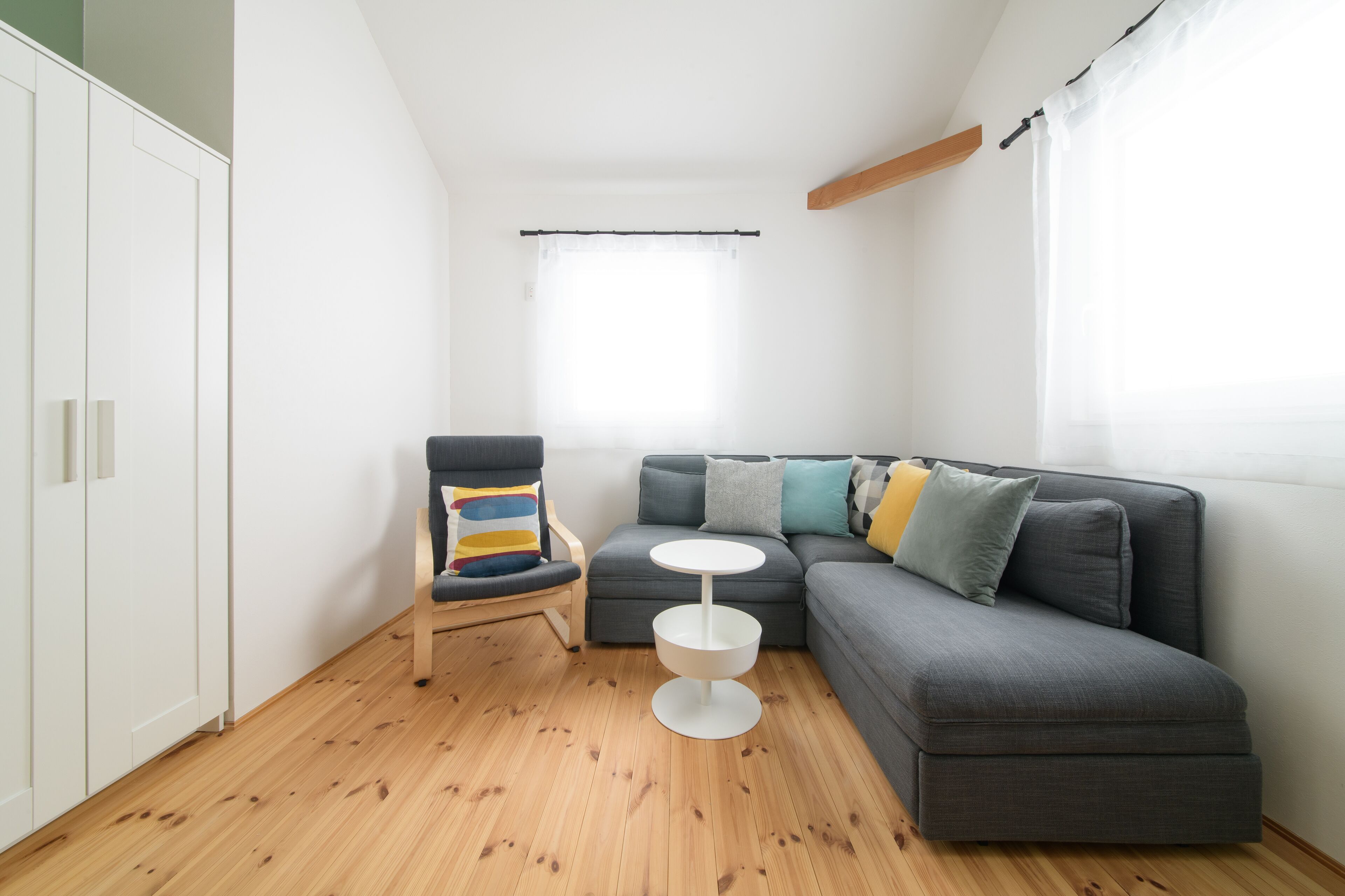 Un espace de vie compact comprenant un canapé gris, une petite table ronde, un plancher en bois et une armoire blanche.