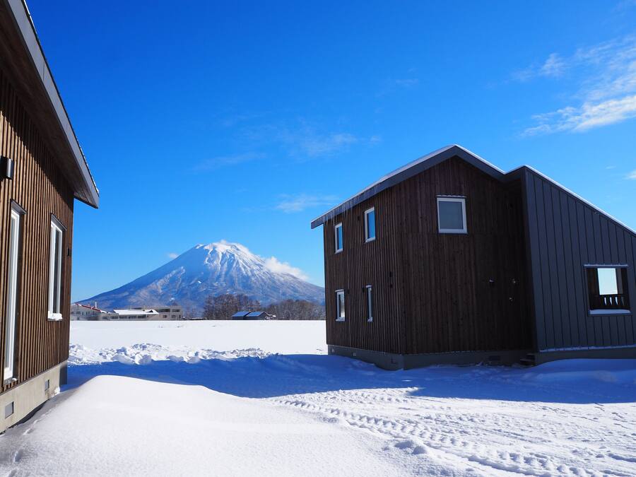 A snow-covered landscape with a mountain in the background and two wooden buildings in the foreground.
