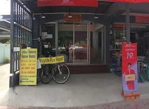 A hostel entrance with a sign for Patone Hostel, a bicycle for rent, and a J&T Express store. - Patone Hostel (Ayutthaya)