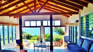A spacious living area with a large window overlooking a lush garden and the ocean. - Makaira Resort (Taveuni Island East)