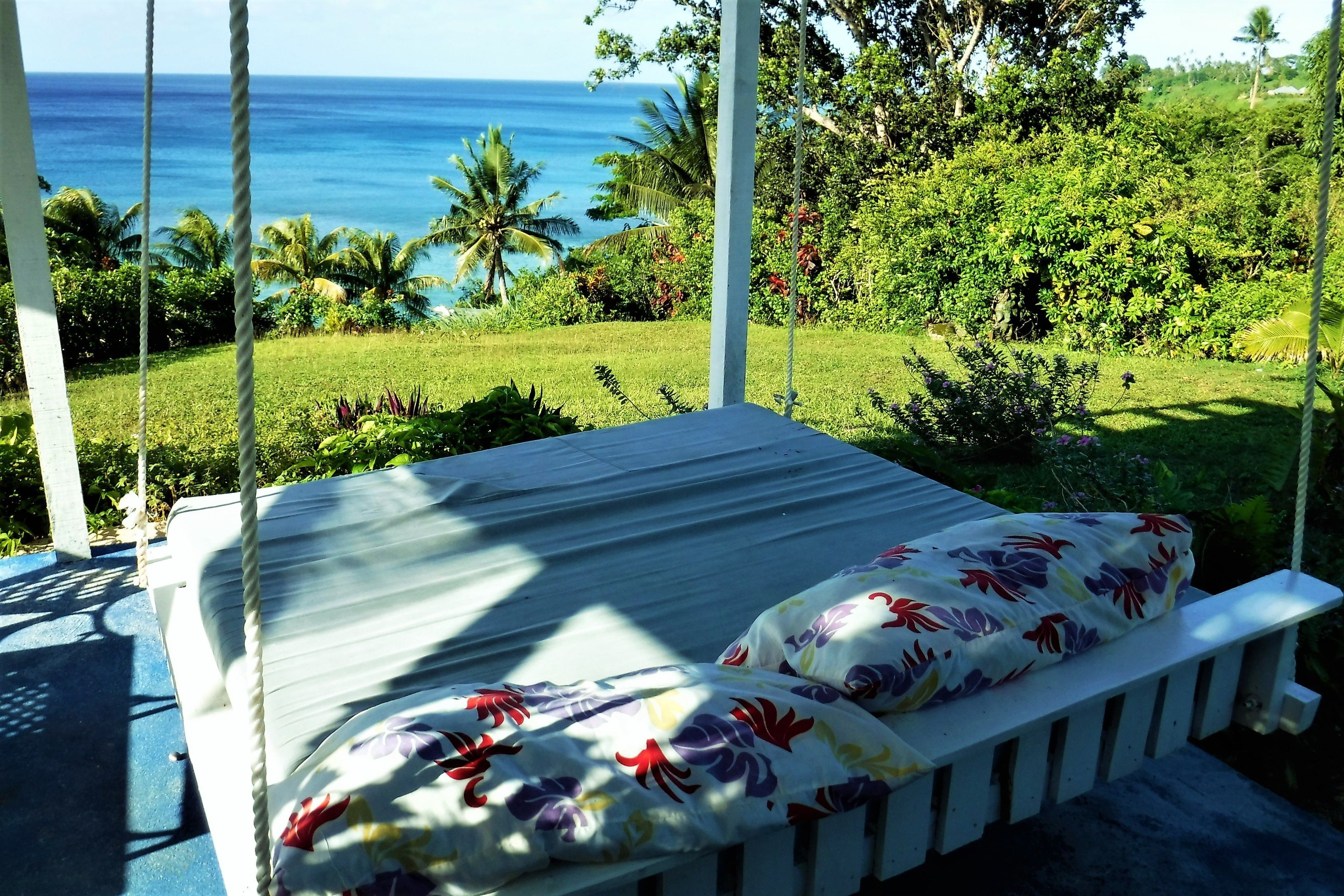 Un hamac, agrémenté d’une couverture à motifs floraux, offrant une vue imprenable sur un jardin luxuriant et l’océan.