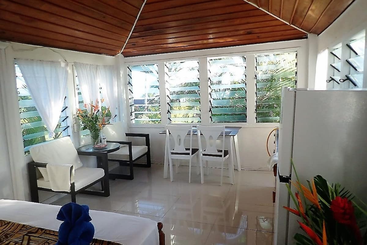 Una habitación con techo de madera, paredes blancas, un comedor con sillas blancas, una mesa y un refrigerador.