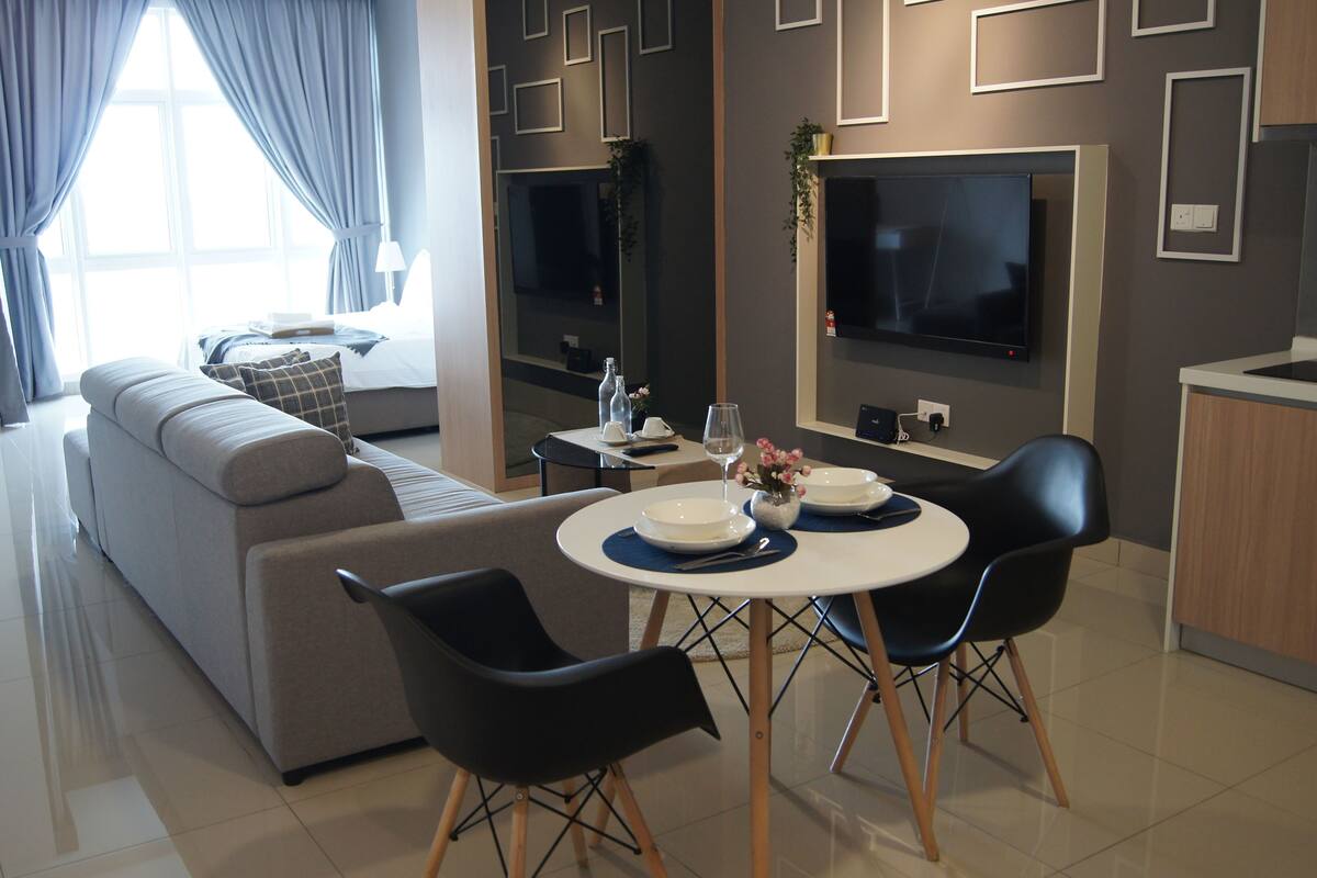 A modern living room with a sofa, a dining table with chairs, a TV, and a kitchen area.