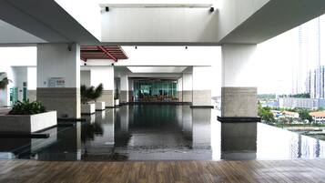 An indoor swimming pool area with a wooden floor, large pillars, and a view of a cityscape in the background.