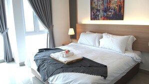 A neatly made bed with white linens, a grey throw blanket, and a tray with folded towels and a rose. - Twin Galaxy Suites (Johor Bahru)