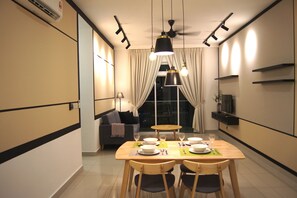 Un espace repas moderne avec une table en bois dressée pour quatre personnes, un canapé et un téléviseur en arrière-plan.