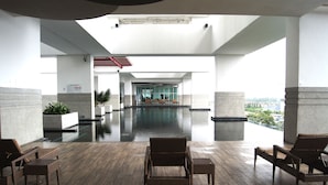 A modern indoor pool area with a view of the city, featuring a wooden deck, wicker lounge chairs, and a glass-enclosed pool. - Twin Galaxy Suites (Johor Bahru)