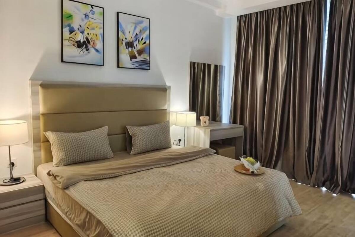 Una habitación de hotel con una cama grande, lámparas de noche, una mesita de noche, un escritorio y una ventana con cortinas.