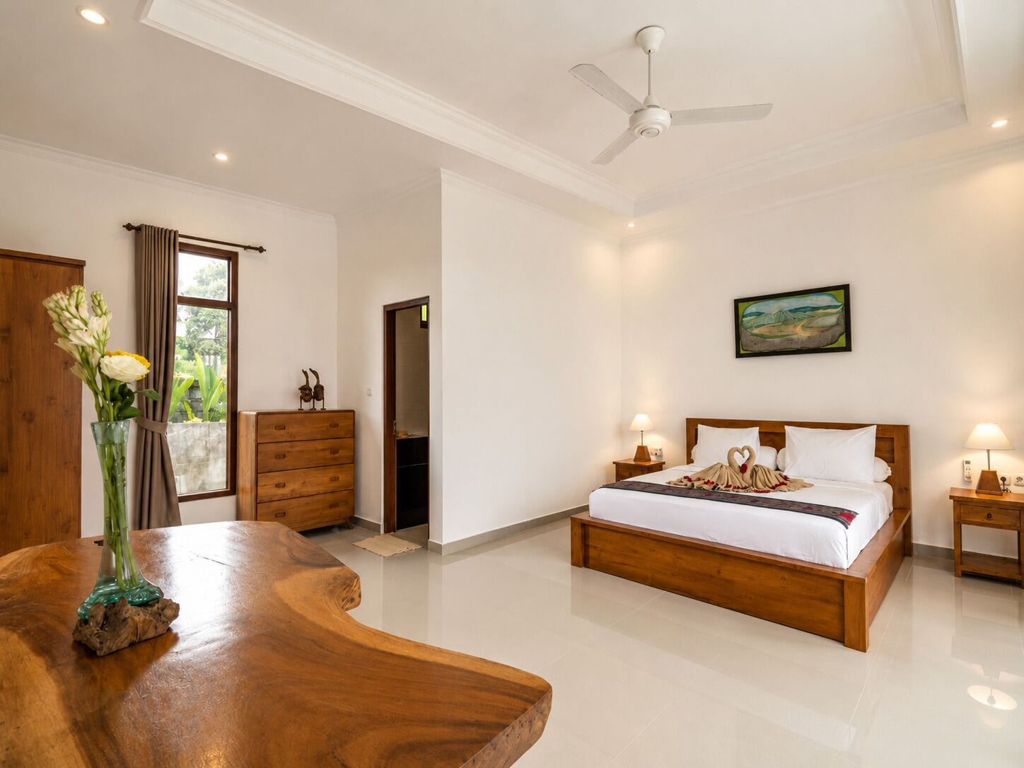 A modern bedroom with a wooden bed, a nightstand, a dresser, a ceiling fan, and a window with curtains.